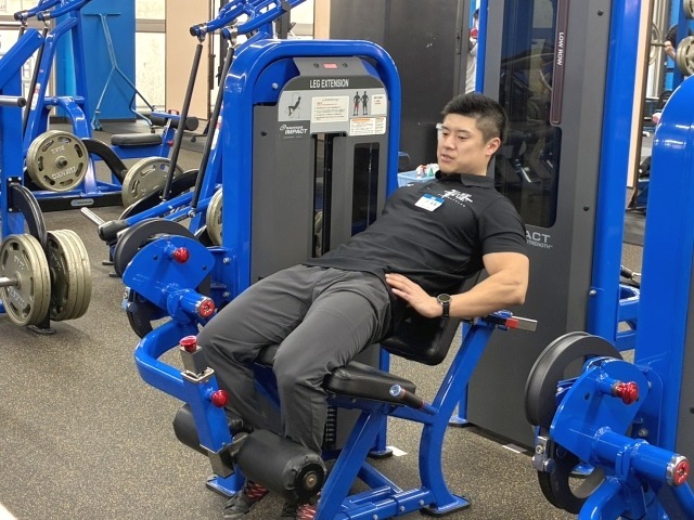 正解はないとした上でバリエーションの一つとして紹介。レッグエクステンションは教科書的なやり方では膝しか動かないが、大腿直筋は膝を伸ばす+股関節屈曲作用があるためレッグエクステンションを多関節種目として扱う。画像は腰が浮いたNG例。